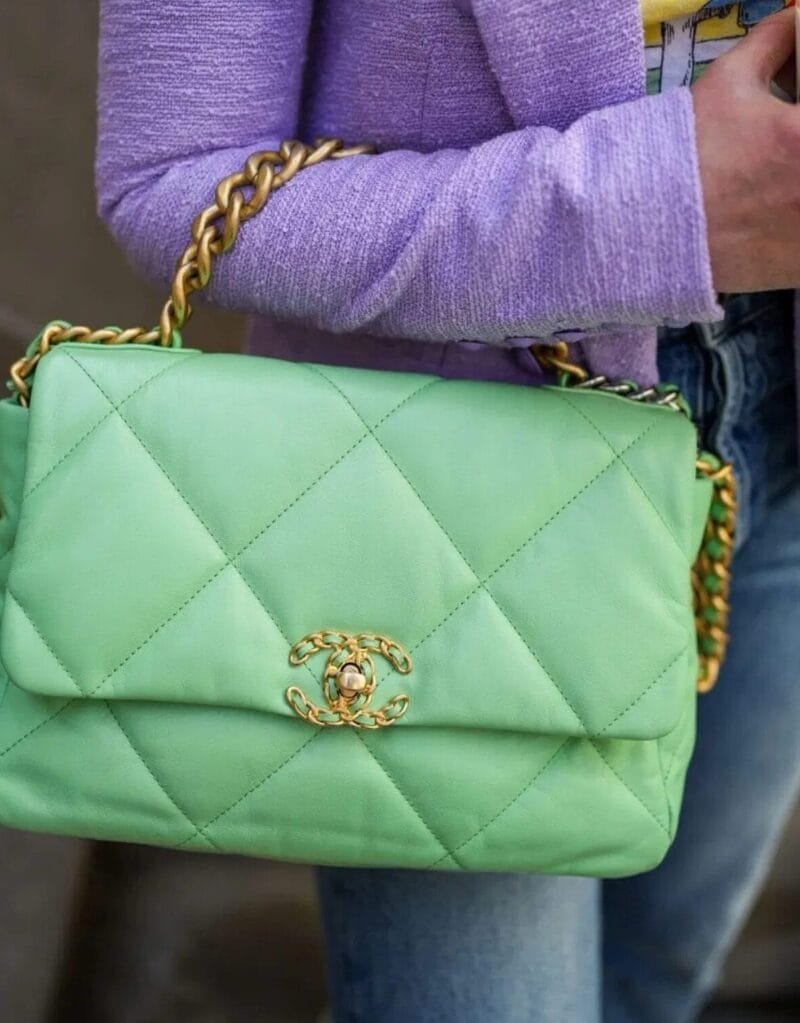 A person in a light purple blazer and blue jeans holds a light green quilted Chanel handbag, highlighting the expert personal styling of Style Reclaimed: Your Transformation Experience.